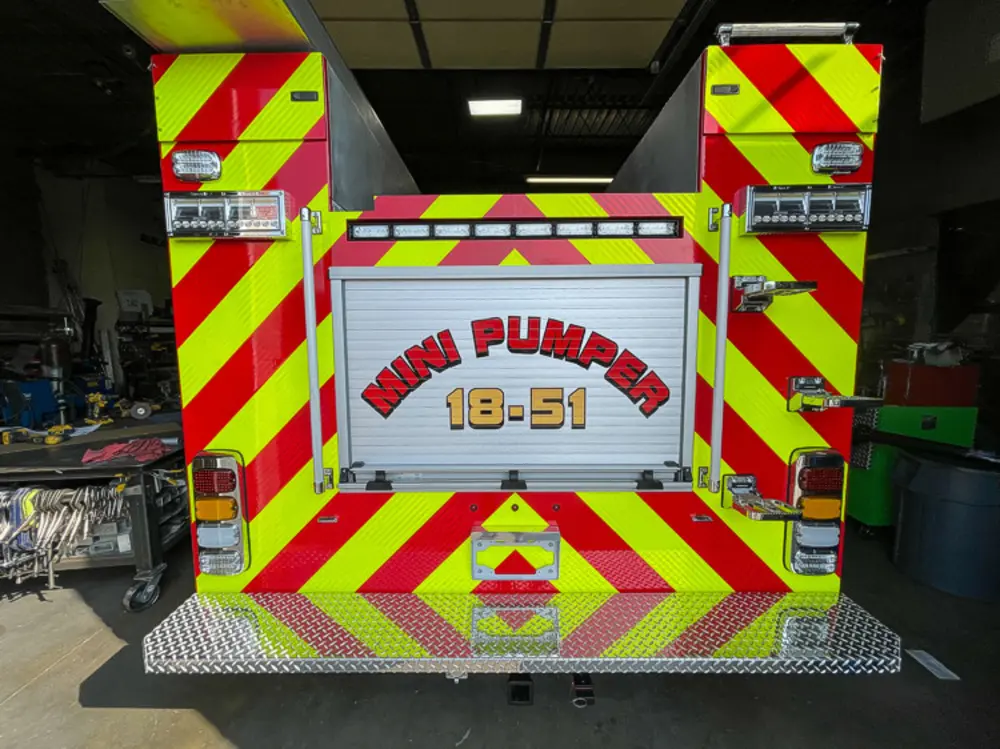 Exterior view of small fire truck showing cab, body compartments, and wheel/tire area.